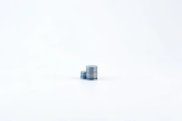 Gráfico de barras ascendente com moedas de dinheiro empilhadas ao lado, em fundo branco.