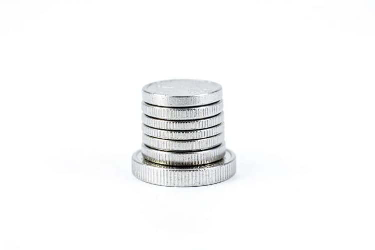 Uma pilha de moedas de dinheiro em cima de uma única moeda, em fundo branco.