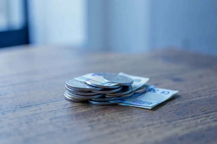 Uma pilha de moedas e notas de dinheiro em cima de uma mesa de madeira, representando custos.