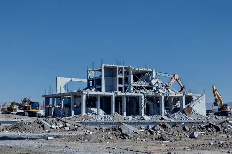 Uma casa sendo demolida parcialmente com uma escavadeira, indicando uma reconstrução completa em vez de uma reforma.