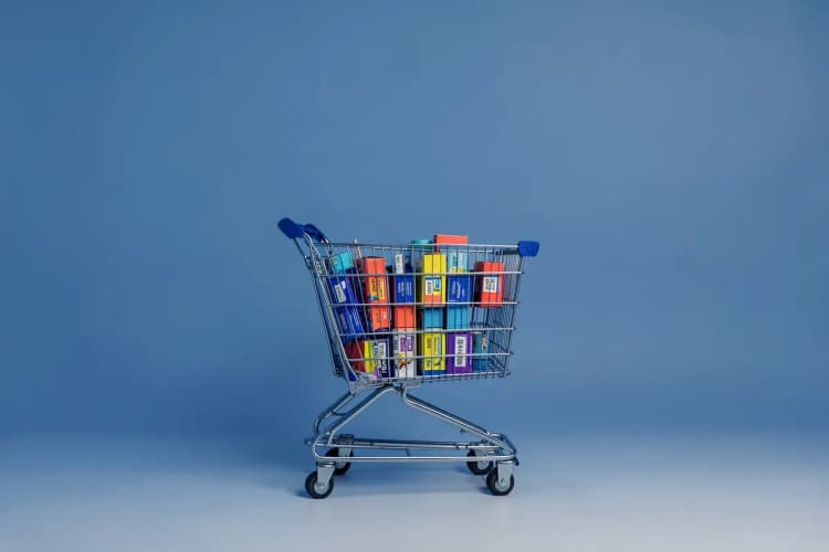 Um carrinho de compras de supermercado cheio de caixas de produtos com etiquetas de preço, em um fundo branco limpo.